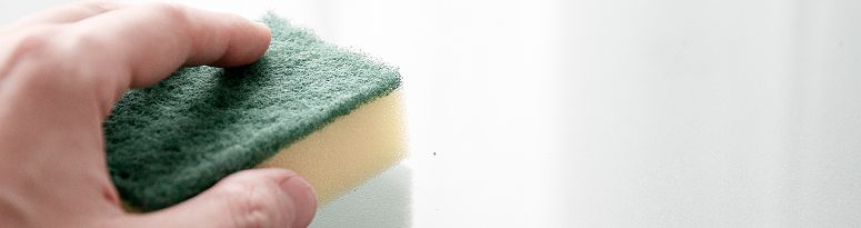 A hand holding a yellow and green sponge, wiping down a white fiberglass planter surface