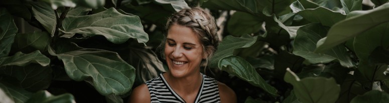 a smiling woman surrounded by dark green leaves of a large plant