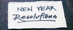 A handwritten note reading “New Year Resolutions” on a small piece of white paper placed on a dark wooden surface