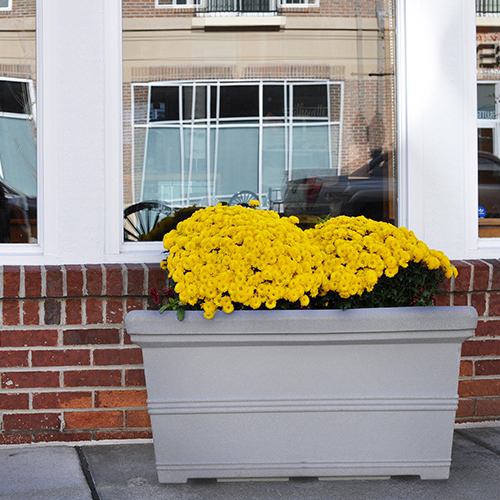 rectangle faux stone planter box with yellow flowers installed in front of storefront window and brick wall