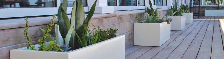 A line of white rectangular fiberglass planters against a building demonstrating how to secure outdoor planters